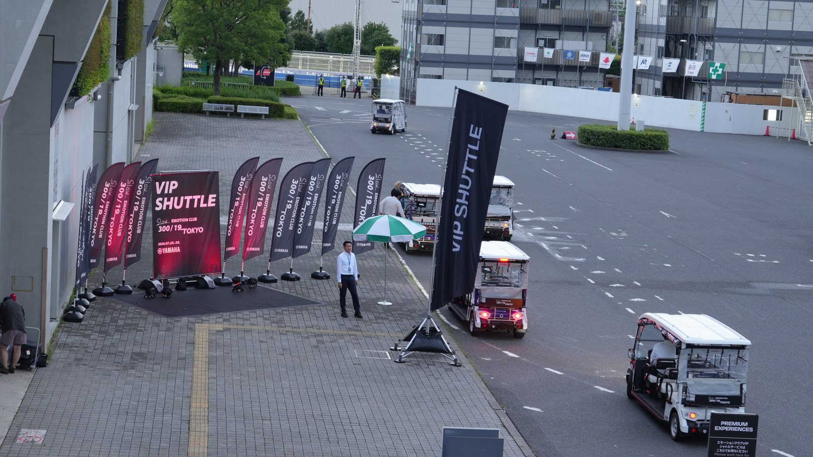 のぼり旗が並ぶ乗降場所に待機するグリスロと、奥の通路を走行する車両