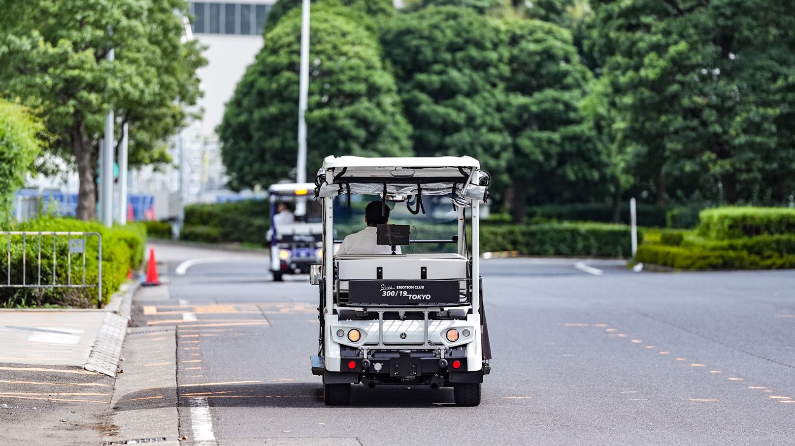 並木道を走る白いグリスロを後方から見た様子。前方にもう1台が走る